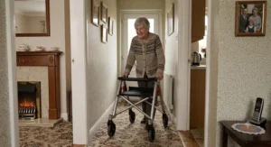 A narrow folding walking frame for travel being used to navigate a cosy British living room hallway safely.