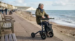 A senior resting comfortably on the built-in padded seat of an all terrain rollator walker parked along a coastal promenade.