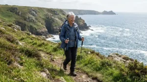 Mature walker using hiking poles for bad knees along the uneven terrain of the South West Coast Path